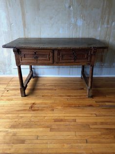 an old wooden desk sitting on top of a hard wood floor next to a wall