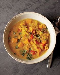 a white bowl filled with soup next to a spoon on top of a gray table