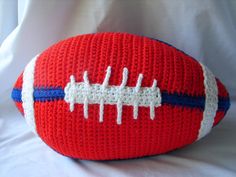 a crocheted red and white football sitting on top of a white sheet,