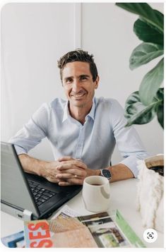 a man sitting at a table with a laptop computer in front of him, smiling