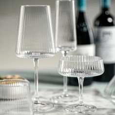 three empty wine glasses sitting on top of a table next to bottles and glassware