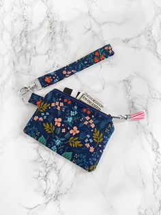 a small blue floral purse with a lanyard and keychain on a marble surface