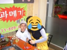 two children sitting at a table in front of a sign with an emoticive face on it