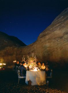 a group of people sitting at a table in the middle of a desert with lights on