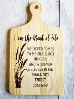 a cutting board with the words i am the bread of life written on it and some brown reeds