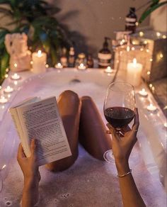 a woman laying down in a bathtub reading a book and holding a glass of wine