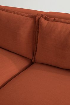 an orange couch with two pillows on it's back and one pillow that is folded over