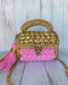 a pink and gold handbag with tassels on the handle, sitting on a white wooden surface