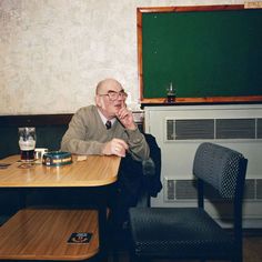 an older man sitting at a table in front of a chalkboard