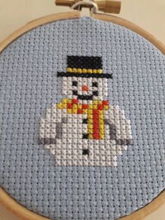 a cross stitched picture of a snowman in a top hat and coat with a cane