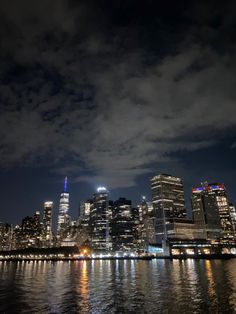 the city skyline is lit up at night with clouds in the sky and lights reflecting on the water