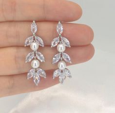 a pair of earrings with pearls and leaves on the end of each earring is being held in someone's hand