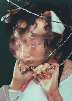 a woman in white shirt holding her hands to her face with barbed wire around her neck