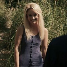 a woman with long blonde hair standing in front of tall grass