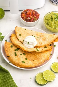 three quesadillas on a white plate with limes and guacamole