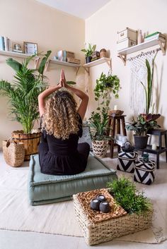 a woman sitting on the floor in front of some potted plants and doing yoga