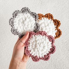 three crocheted coasters are being held by a person's hand on a white surface