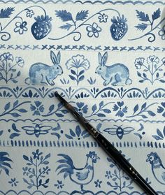 a pen sitting on top of a blue and white wallpaper with rabbits, flowers and leaves