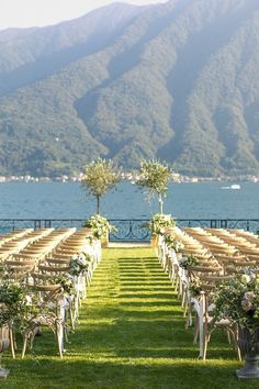 an outdoor ceremony setup with rows of chairs and flower arrangements on the grass by the water