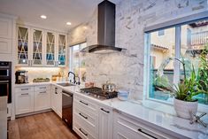 a kitchen with white cabinets and marble counter tops, an open window to the backyard