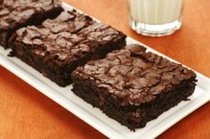 three brownies on a white plate next to a glass of milk and a drink