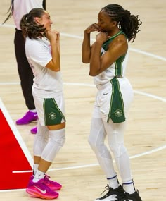 two female basketball players standing next to each other with their hands on their mouths and looking at each other