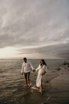 a man and woman holding hands walking in the water on a beach at sunset or sunrise