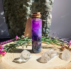 a glass bottle filled with purple liquid sitting on top of a wooden table next to crystals