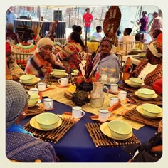 a group of people sitting around a table with plates and cups on it, all dressed in african clothing