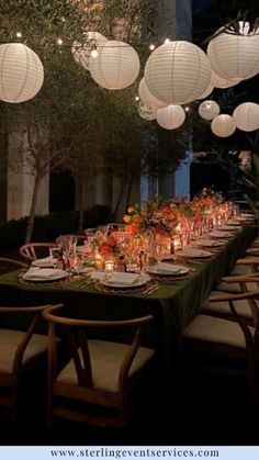 a long table with paper lanterns hanging from it's ceiling and place settings on the tables