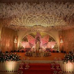 an elaborately decorated stage set up for a wedding ceremony with flowers and petals on the ceiling