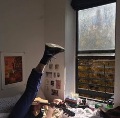 a person laying in bed with their foot up on the window sill while holding an umbrella