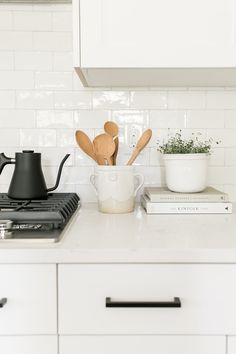 a white kitchen with wooden utensils in a mug and books on the counter