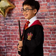 a young boy wearing glasses and holding a harry potter wand in front of a brick wall