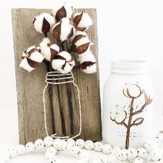 some cotton flowers are in a mason jar next to a white bead necklace on a table