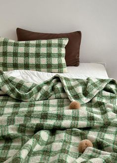 an unmade bed with green and white checkered blankets on it, two teddy bears under the covers