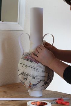 a woman is making a vase out of newspaper