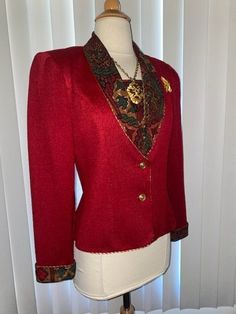 A smart cropped blazer jacket done in red textured fabric. The collar and sleeve cuffs both show a portion of the inside lining which is a different multicolor fabric. V neck opening that also includes a swatch of the same fabric when buttoned in, creates what look like there is a shirt underneath. You do not have to button it in if you desire A different look. There are touches of gold here and there along with gold buttons in front. Being that this is a vintage item from the 1980's there is also shoulder pads. Very classic look and it looks amazing over a black dress or with jeans and heels. Necklace and pins not included This jacket is in great condition. No flaws It's a poly rayon fabric. I believe this best would fit a sz M however please see measurements below. All measurements are t Christmas Formal Fitted Outerwear, Fitted Formal Christmas Outerwear, Fitted Formal Outerwear For Christmas, Vintage Red Party Blazer, Red Holiday Blazer With Long Sleeves, Red Long Sleeve Holiday Blazer, Holiday Red Long Sleeve Blazer, Vintage Red Blazer For Formal Occasions, Fitted Vintage Red Blazer