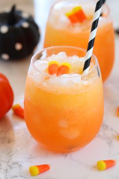 two glasses filled with orange liquid and candy corn on the rim, sitting on a marble table