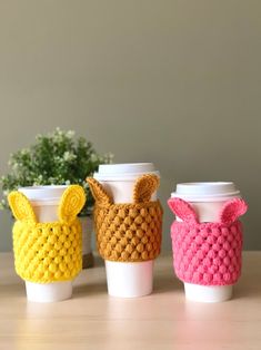 three coffee cups with knitted bunny ears on them, sitting next to each other