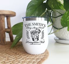 a white coffee cup sitting on top of a table next to a potted plant