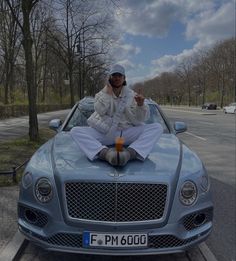 a man sitting on the hood of a car with his thumbs up in front of him