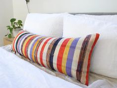 a bed with white linens and colorful striped pillows on it's headboard