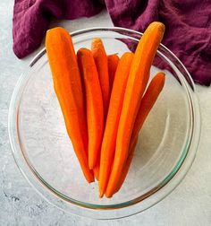 some carrots are in a glass bowl on a white tablecloth and purple cloth