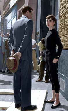 a man standing next to a woman in front of a building with a hat on her head