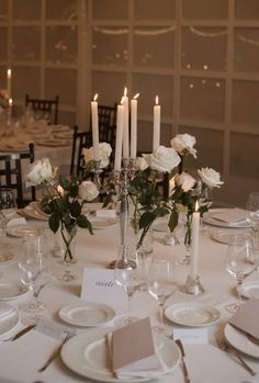 the table is set with white plates and silverware, candles and flowers in vases