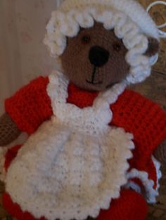 a crocheted teddy bear wearing a red and white dress with an apron on