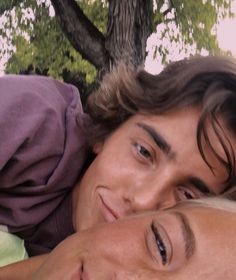 two young men laying next to each other under a tree with their eyes close together