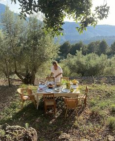 a man sitting at a table in the middle of an olive grove with food on it