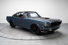 an old blue mustang sitting on top of a cement floor next to a white wall